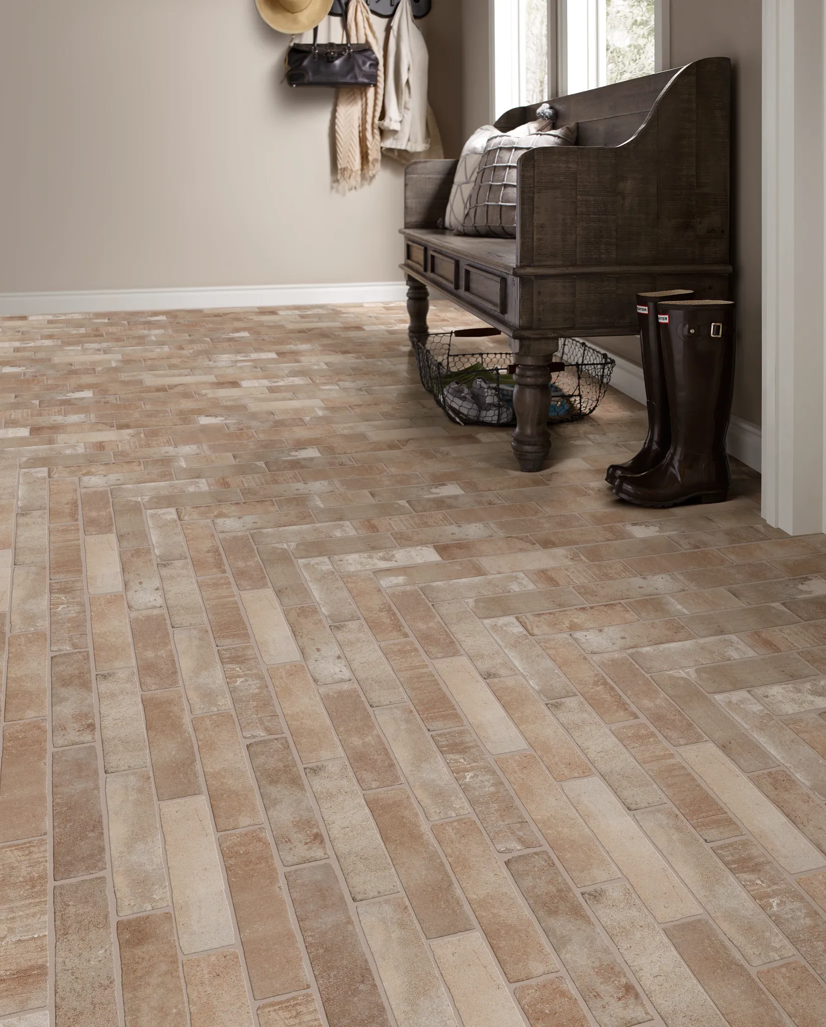 Rustic brick-style flooring in a neutral-toned room with a dark wooden bench and boots