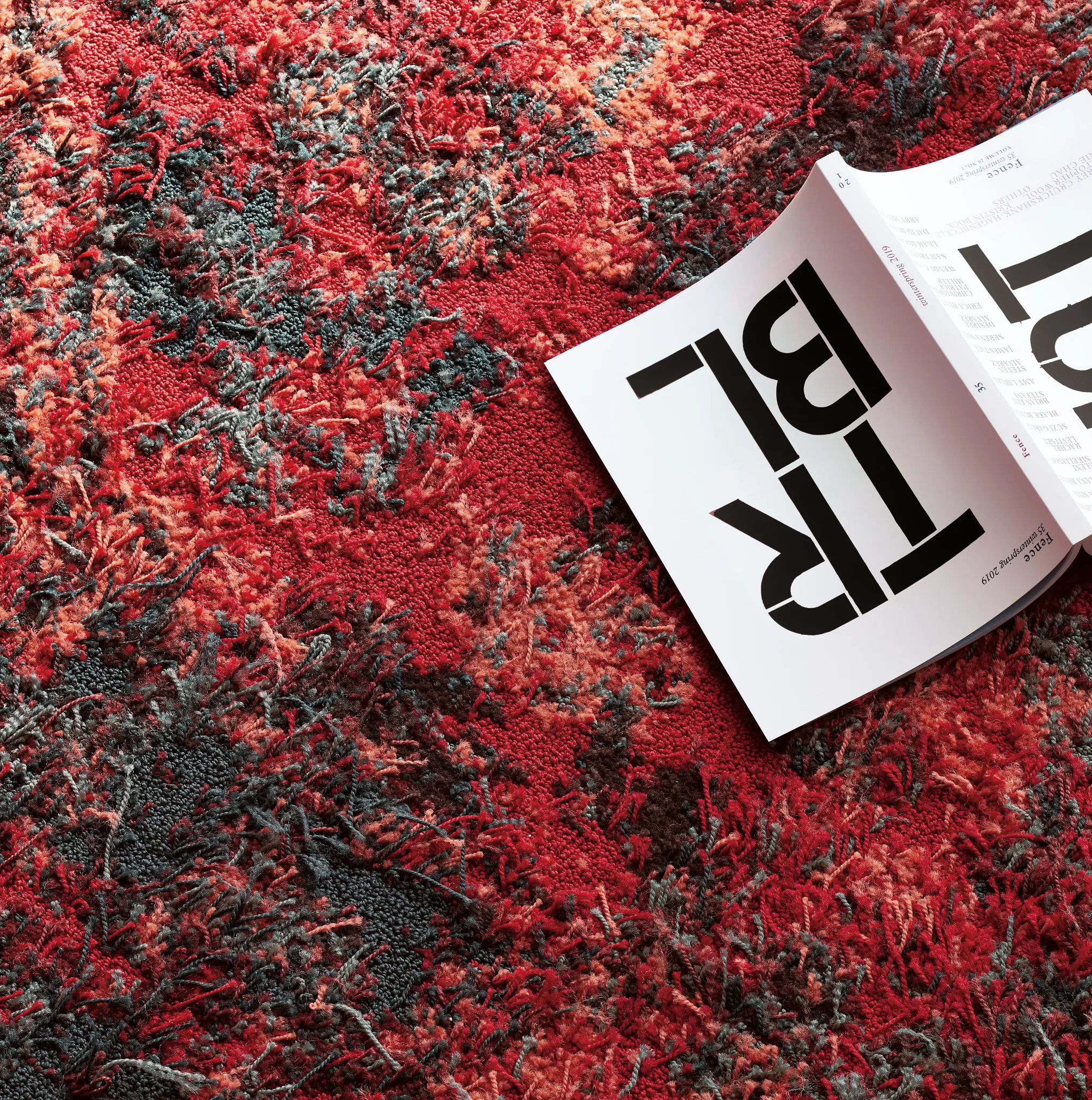 Close-up of a vibrant red, orange, and black textured commercial carpet with a magazine partially visible