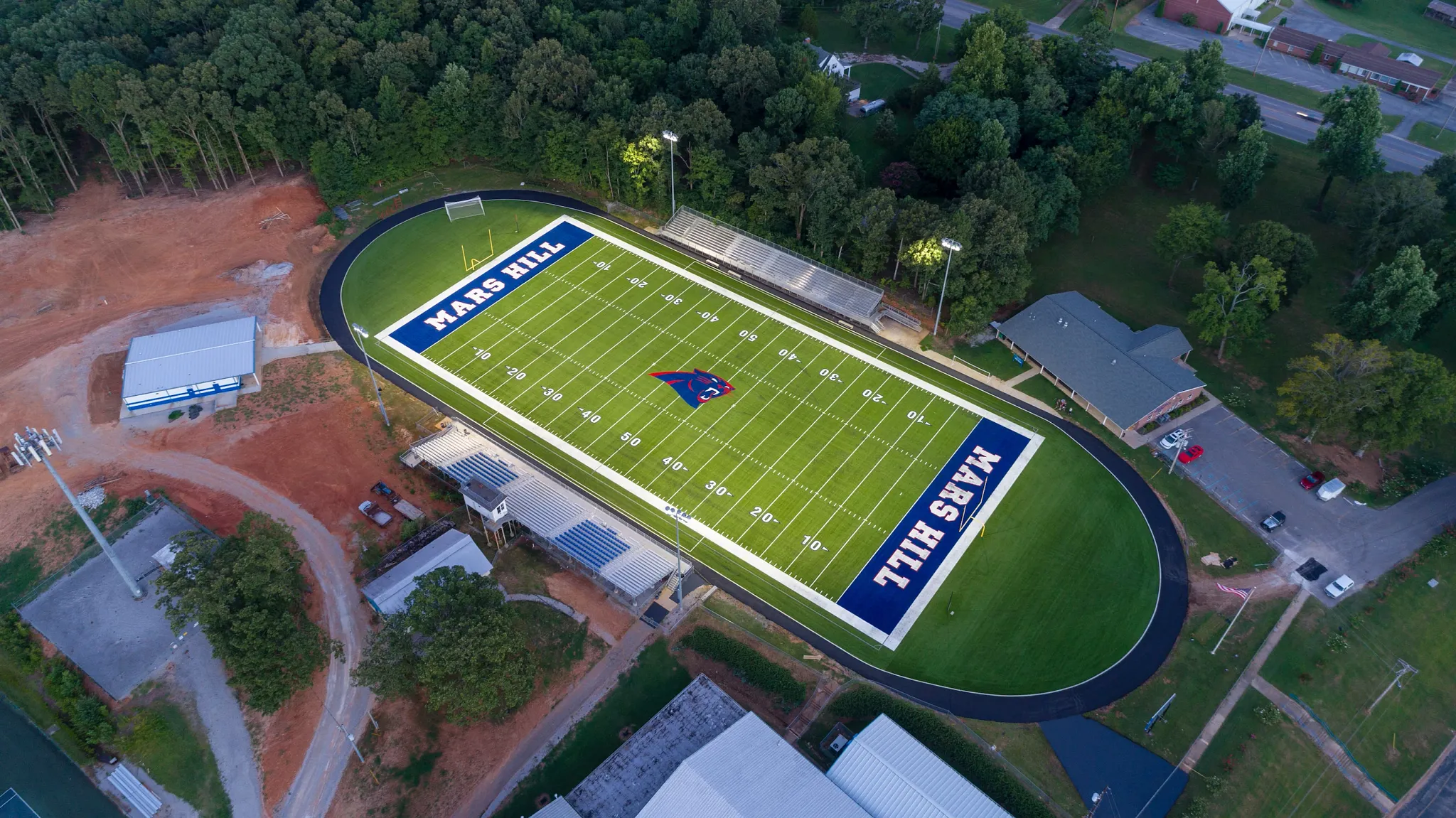 Aerial view of a football field with artificial turf surrounded by trees and buildings