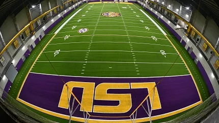Artificial Turf Field in Indoor Sports Facility with LSU Branding Indoor sports facility with artificial turf field featuring LSU logo and purple and yellow end zones