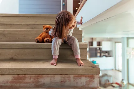 Wood-look LVP flooring on stairs with child and teddy bear in modern home Child sitting on stairs with wood-look luxury vinyl plank flooring and teddy bear