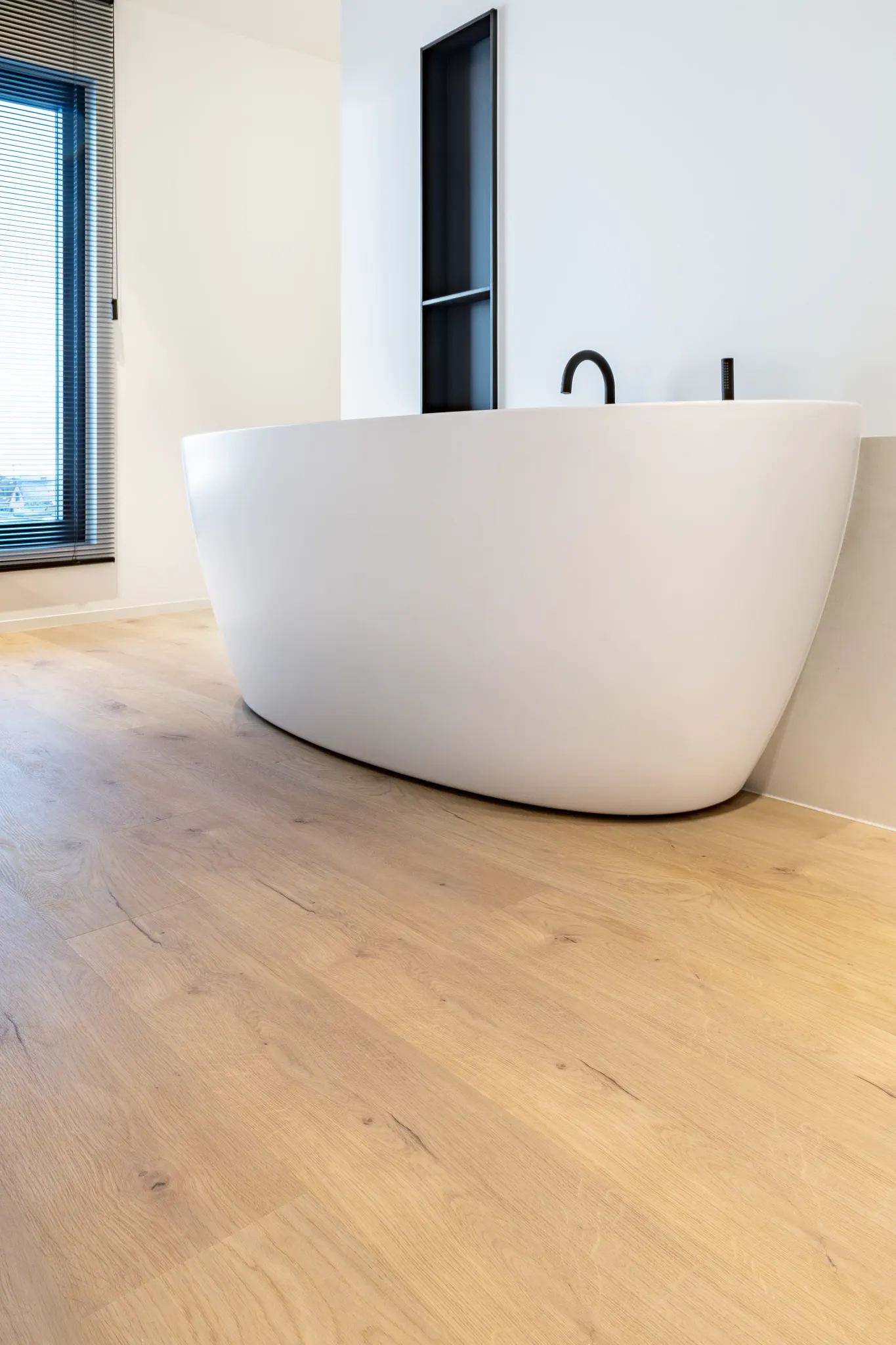 Light oak flooring in a modern bathroom with freestanding tub