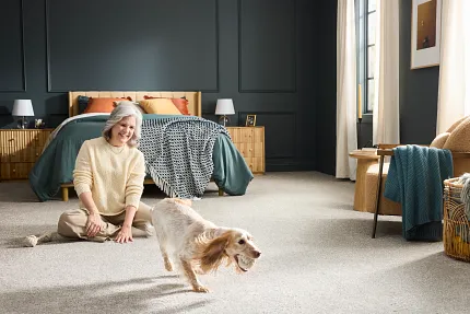 Comfortable and durable carpet flooring for a cozy home environment. Cozy bedroom with durable carpet flooring, featuring a playful dog and a person enjoying the homely atmosphere.