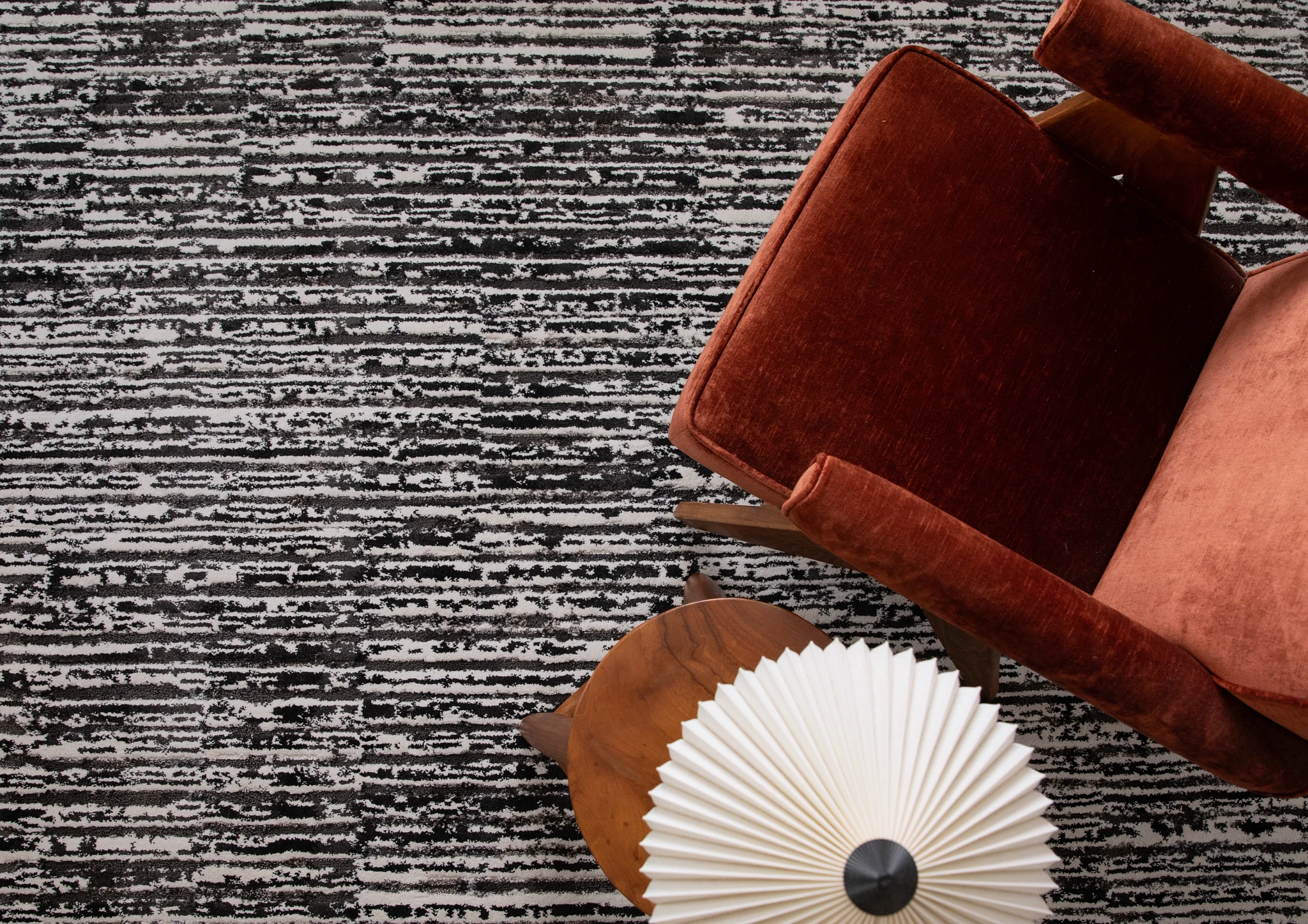 Close-up view of textured black and white carpet with vintage brown chair and decorative paper fan