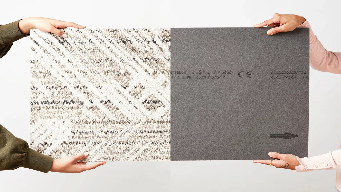 Person holding a Common Thread carpet tile beside its EcoWorx backing, showcasing sustainable flooring construction and material transparency.