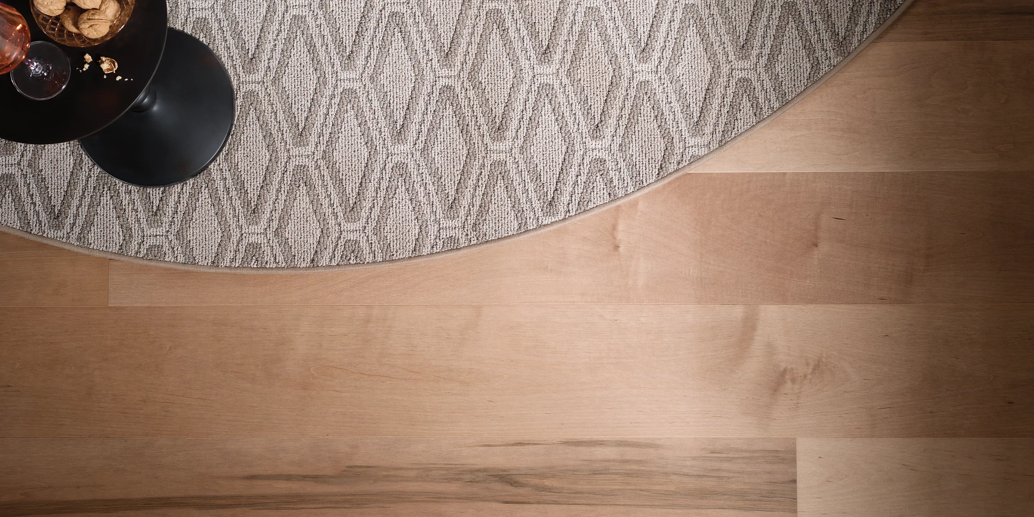 Light hardwood flooring with a round beige and gray patterned carpet