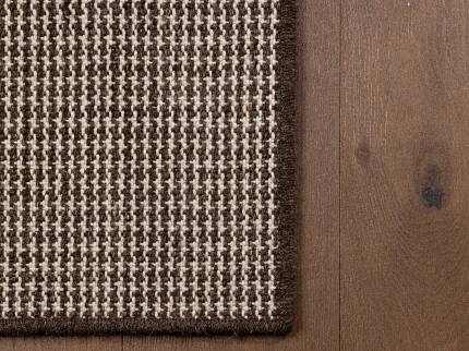 100% Wool Carpet Swatch in Brown and Beige Houndstooth Pattern Close-up of 100% wool carpet swatch in brown and beige houndstooth pattern on wooden floor
