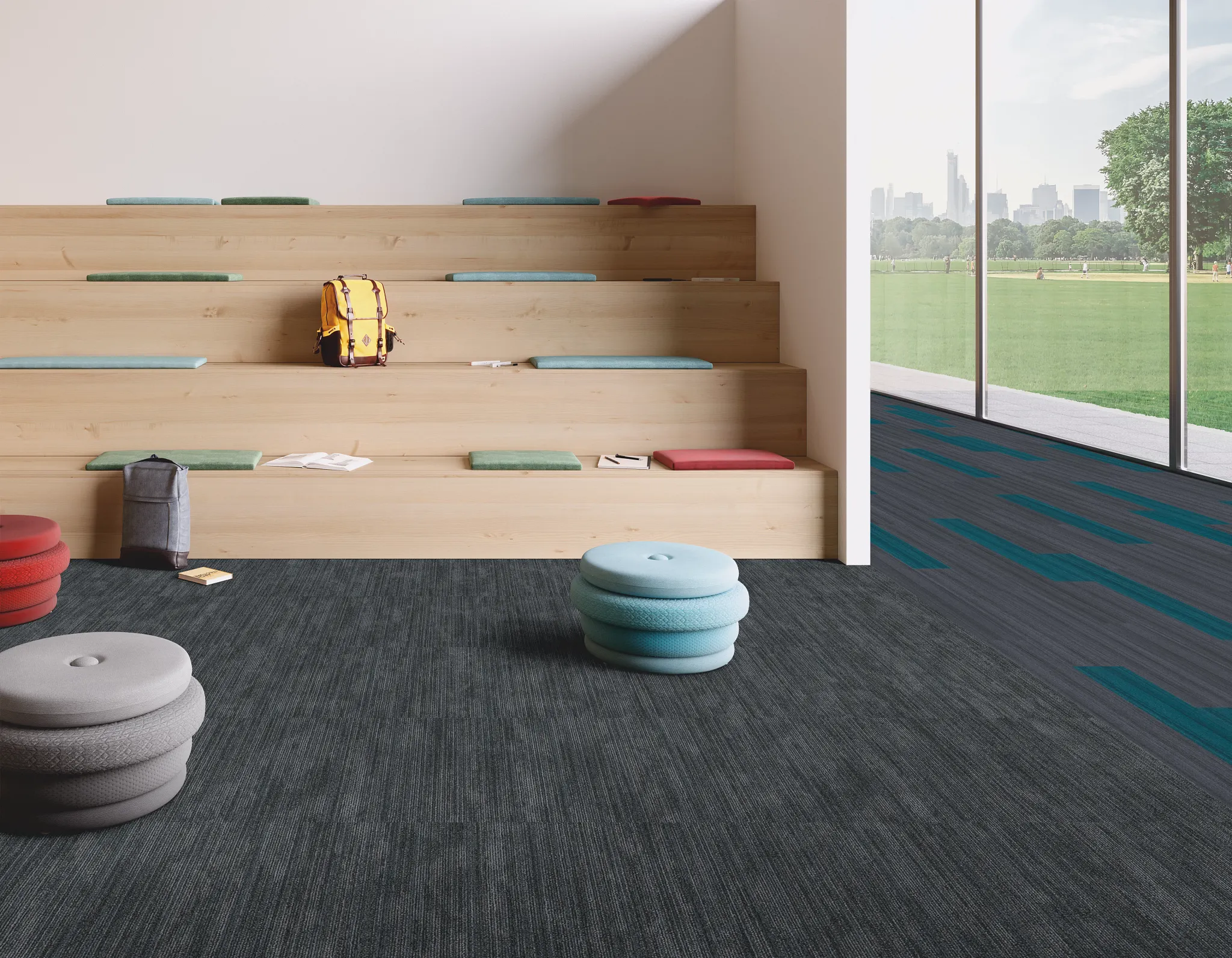 Modern education facility with tiered wooden seating and colorful cushions, featuring dark commercial carpet tile flooring and large windows overlooki