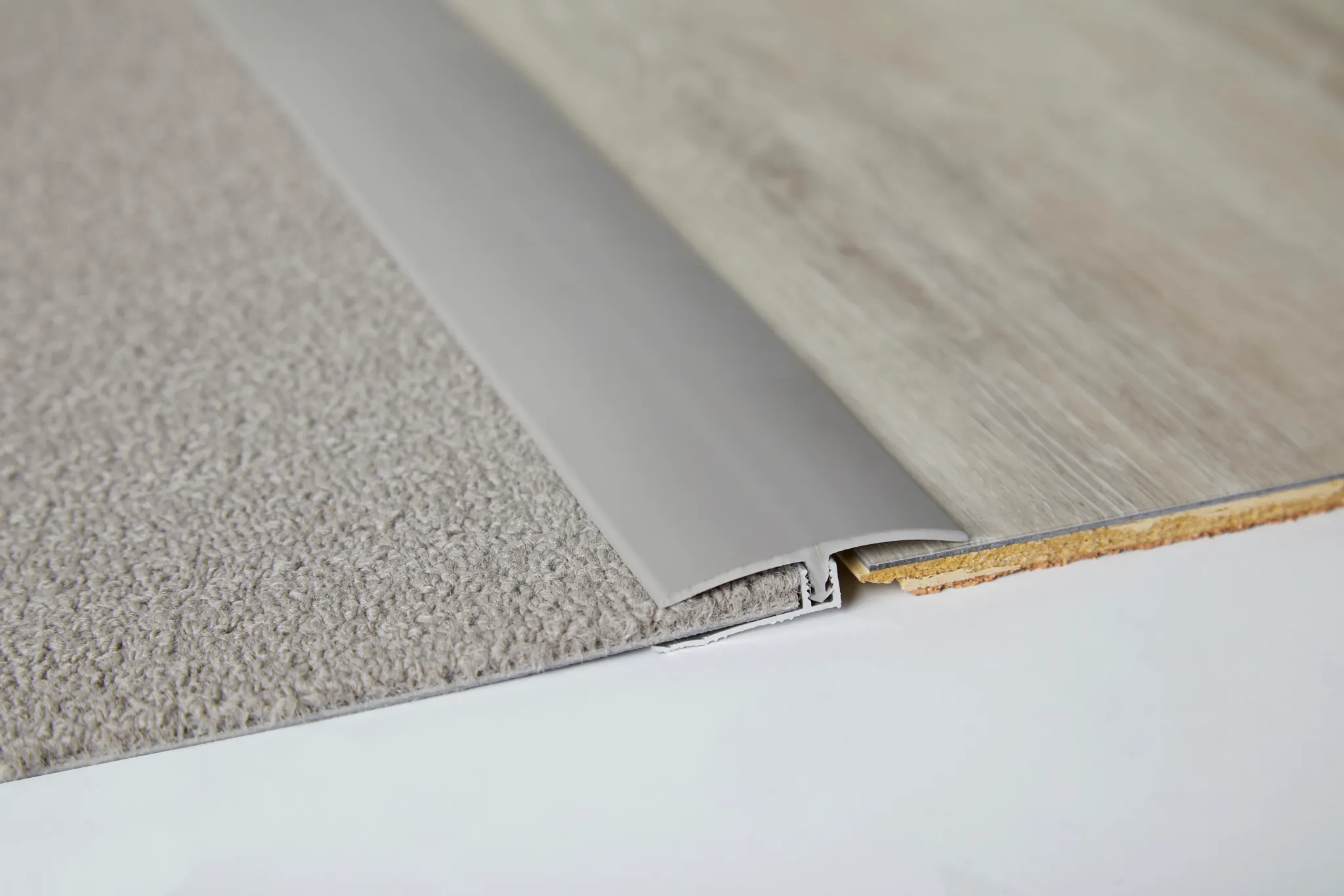 Close-up of flooring transition between beige carpet and light wood-look flooring with metal trim