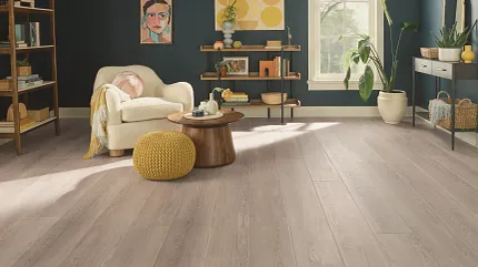 This COREtec product features Soft Step, our newest attached underlayment. living room with light wood look vinyl plank and quirky artwors with cream easy chair yellow poof ottoman and small side table
