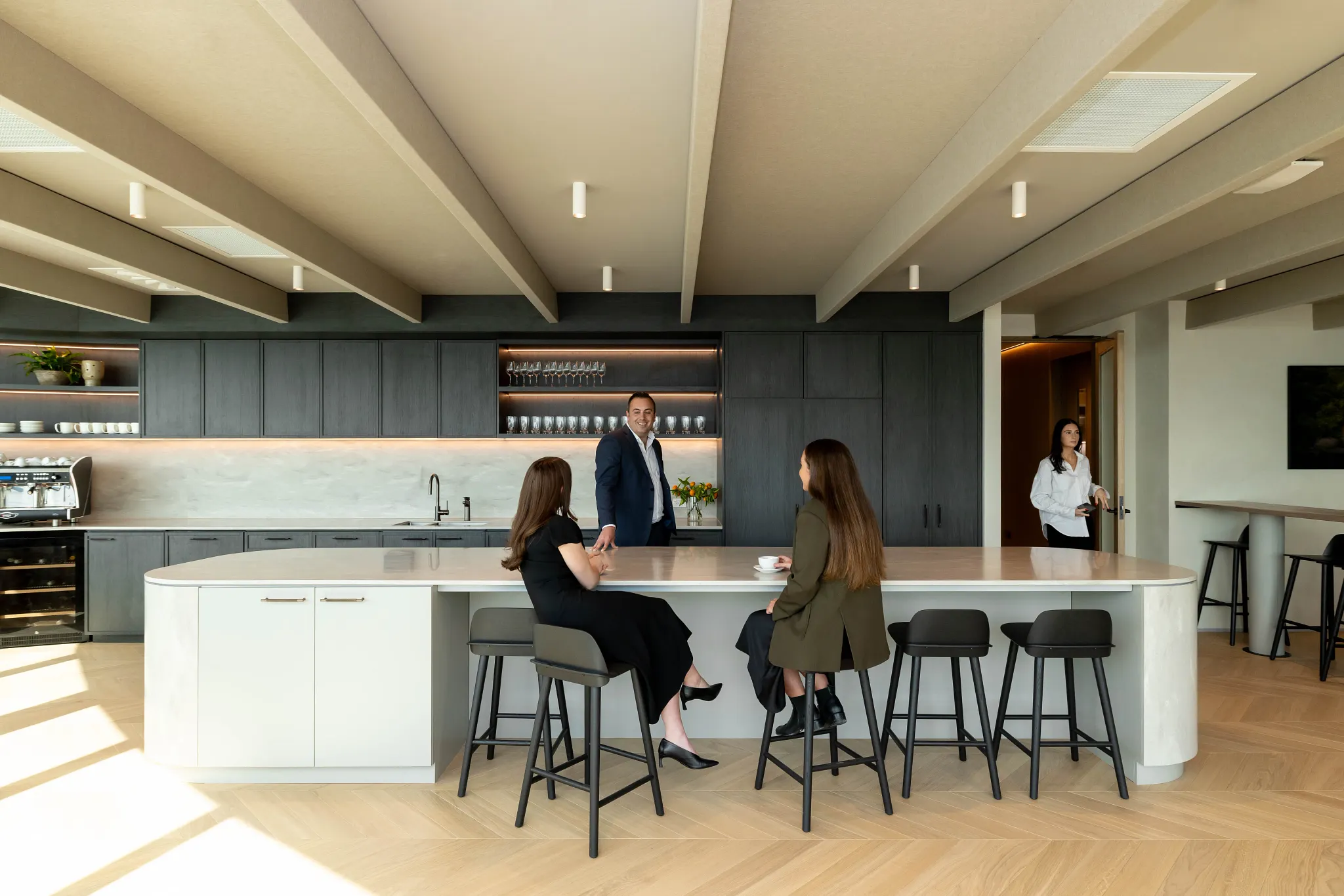 Modern office kitchen with light wood flooring and people interacting