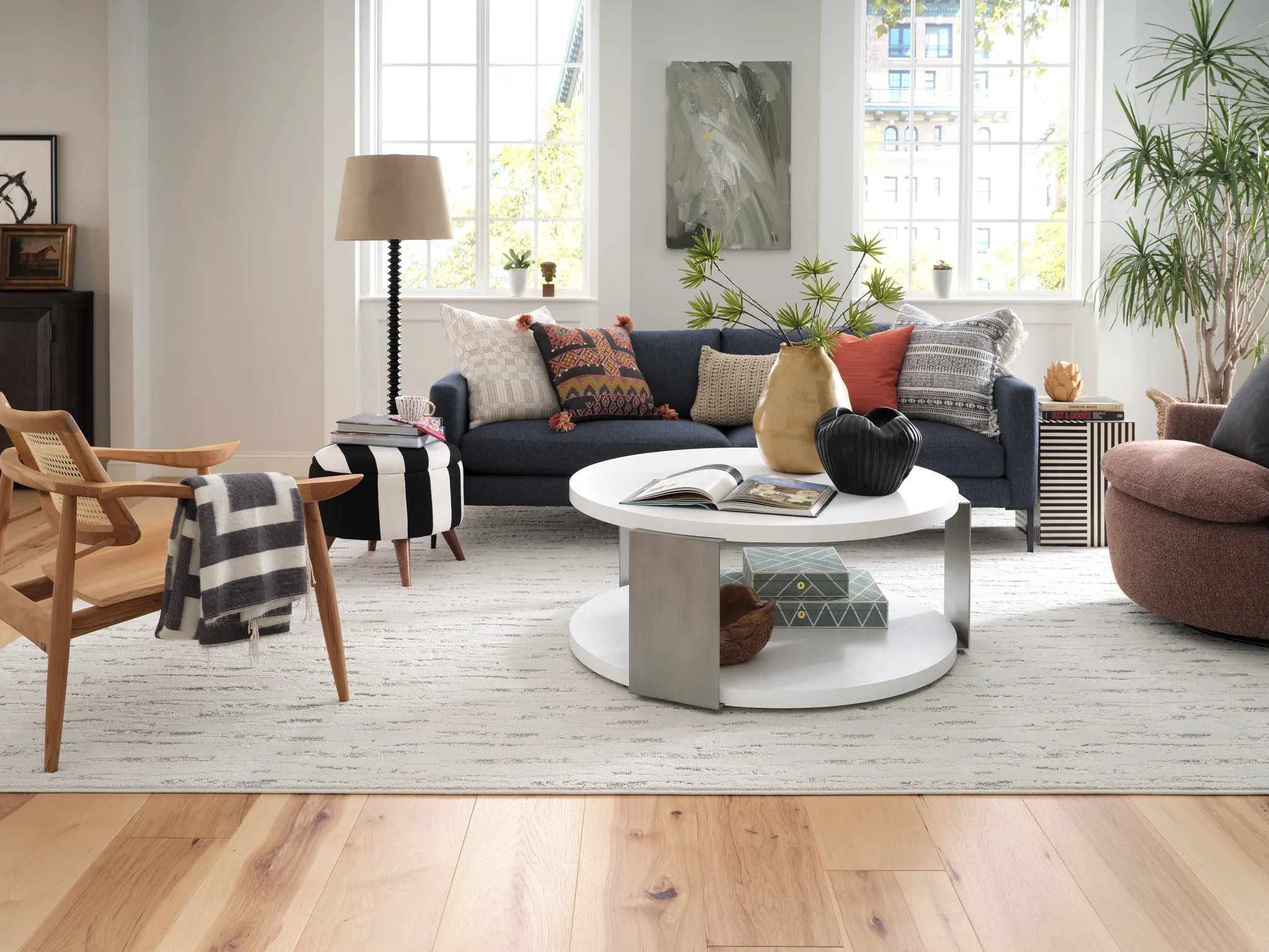 Modern living room with natural wood flooring, featuring a navy sofa, patterned cushions, and a white round coffee table