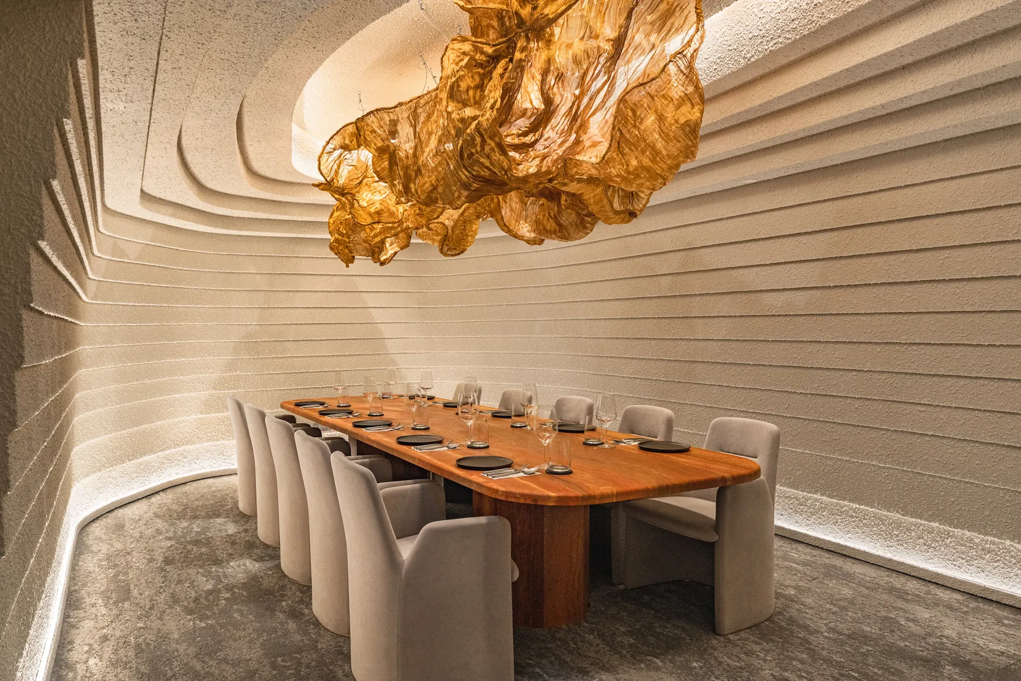 Elegant dining room with a long wooden table, beige upholstered chairs, and a unique ceiling sculpture