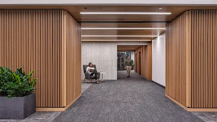Contemporary Workplace Hallway with Commercial Carpet Tile Flooring Modern workplace hallway with commercial carpet tile flooring, featuring a woman seated and a man walking, surrounded by wooden paneling and indoor plants
