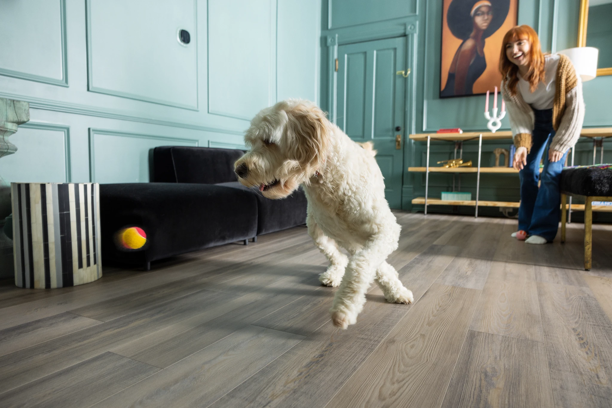 Luxury vinyl plank flooring in a modern living room with a playful dog and a woman, featuring Coretec Mineral Core construction, 47.64x7.6 inch dimensions