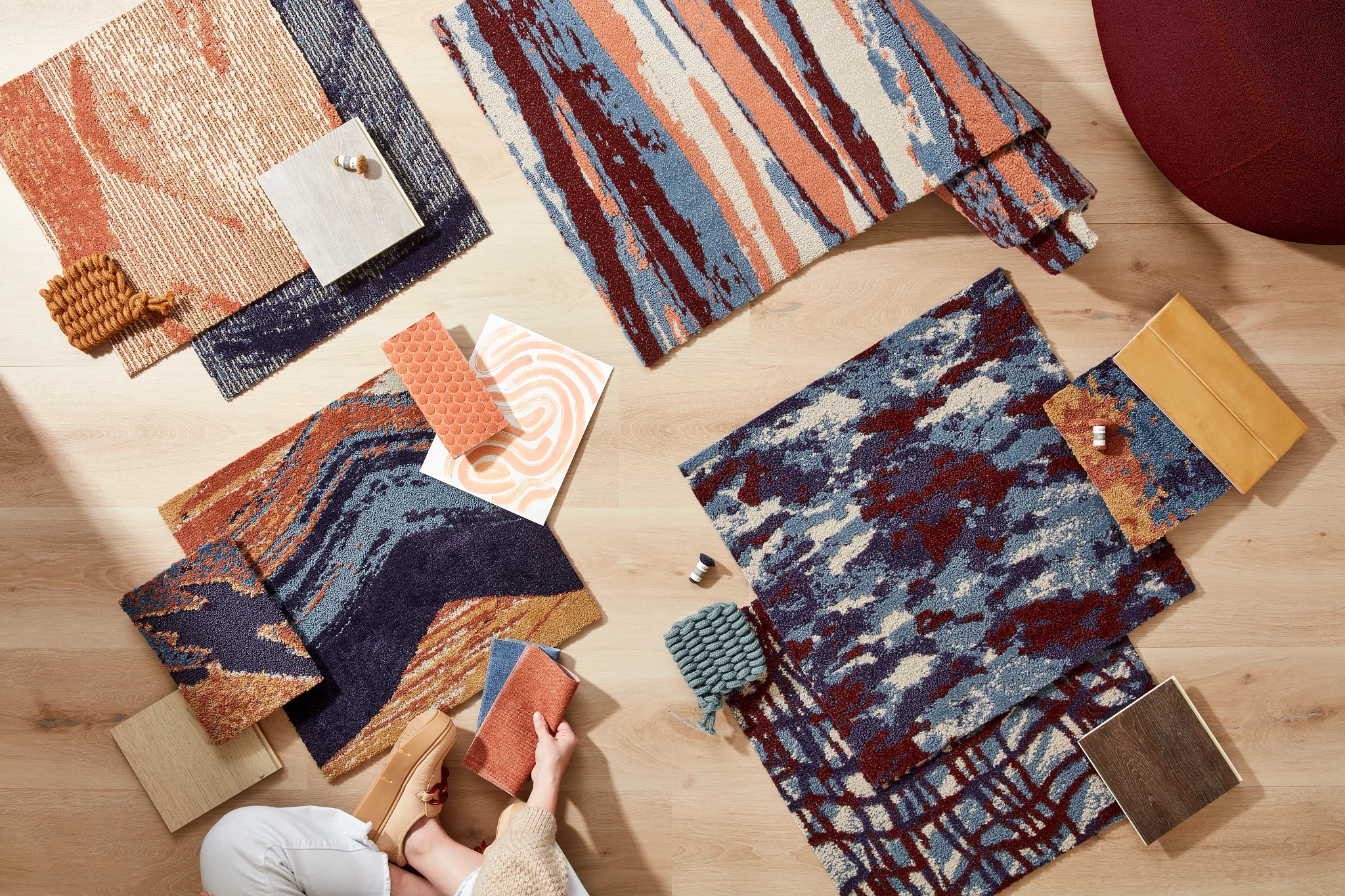 Assorted colorful carpet swatches on light wood flooring with a person holding a sample