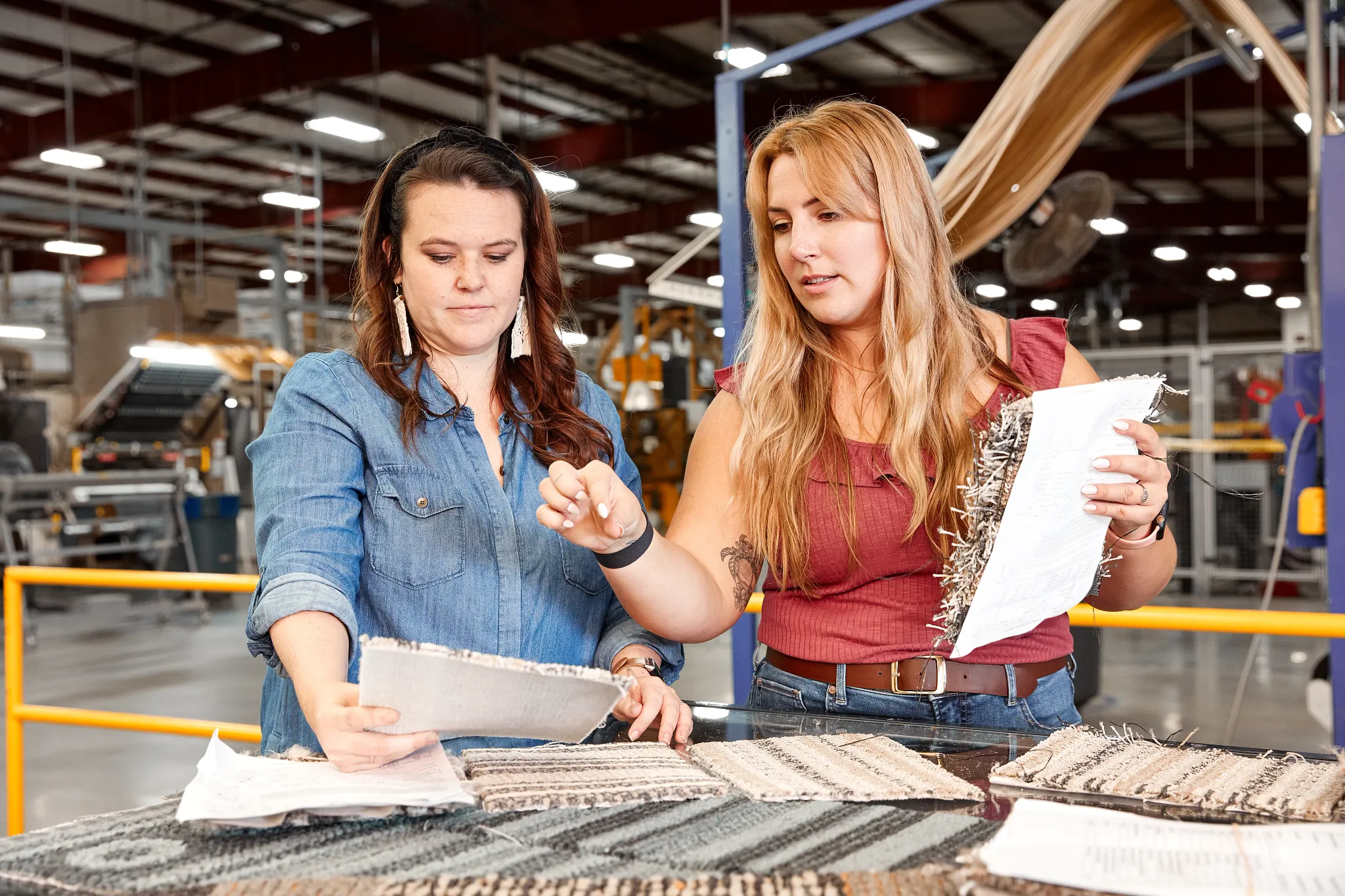 Two women examining commercial carpet tile samples in a manufacturing facility