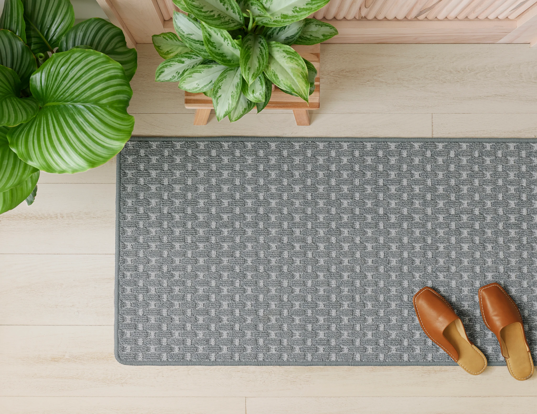 Top view of a gray patterned carpet runner in a home entryway with wooden shoes and green potted plants