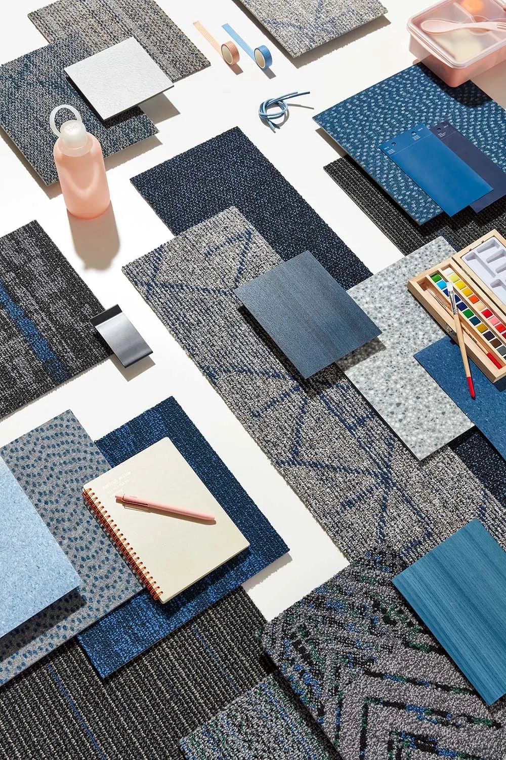 Assorted blue and gray commercial carpet tile swatches with art supplies on a white background