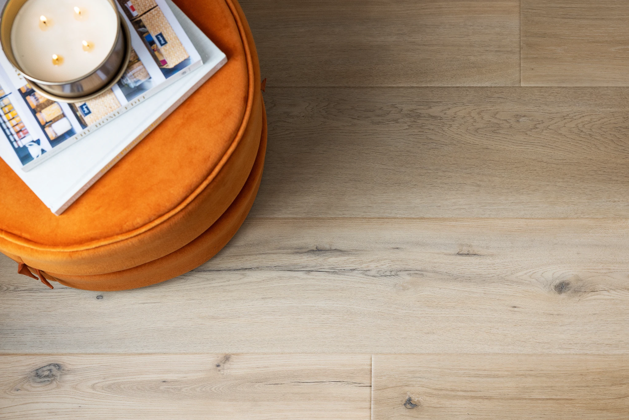 Light wood look luxury vinyl plank flooring with orange ottoman and magazines