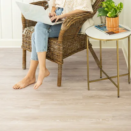Light Wood Look Vinyl Flooring in Residential Setting - Coretec WPC 48x7 inch Woman sitting on wicker chair using laptop on light wood look vinyl flooring