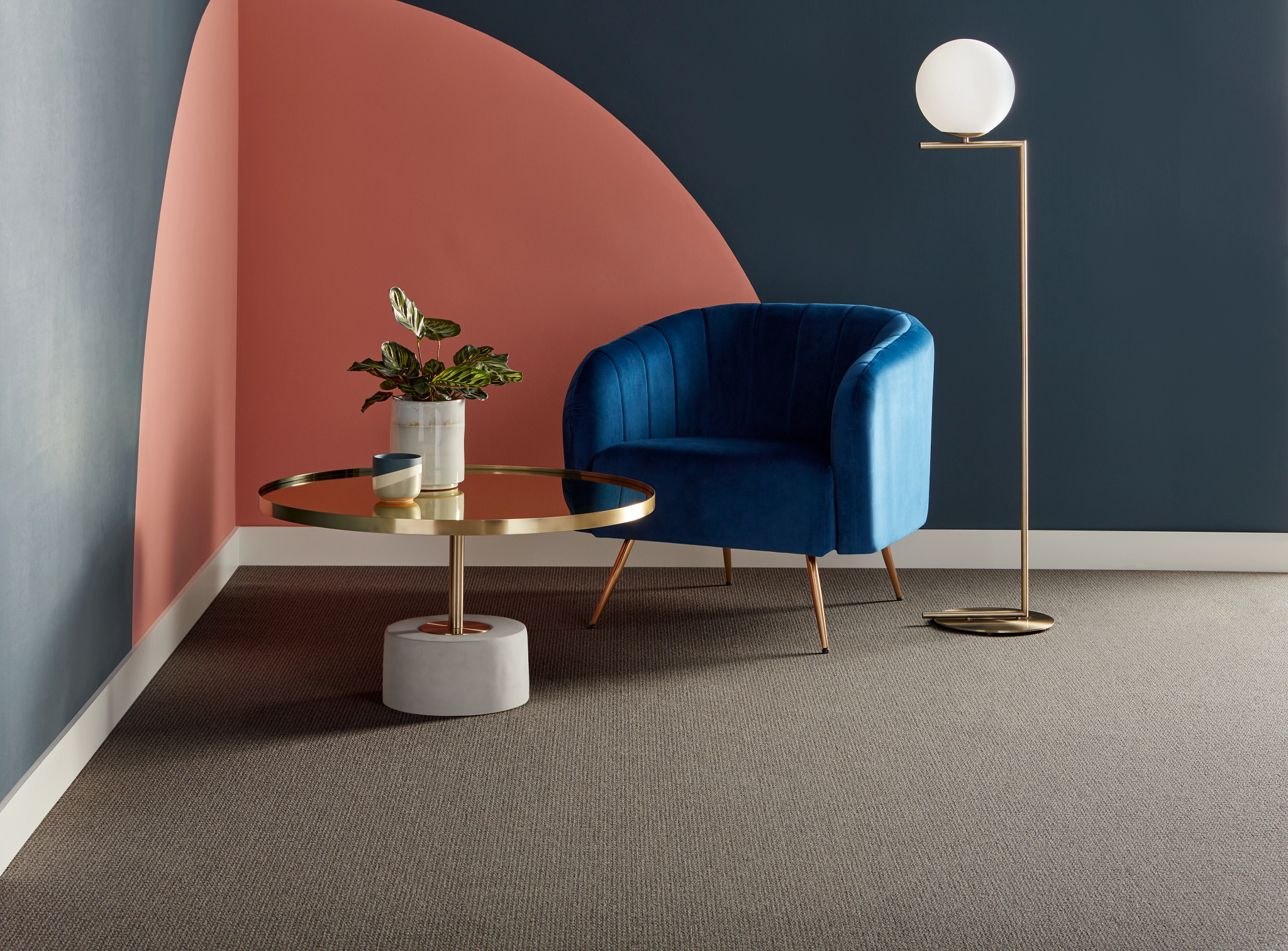 
  "room with gray carpet floor blue velvet chair gold floor lamp and round coffee table against a dark blue and coral wall"
)