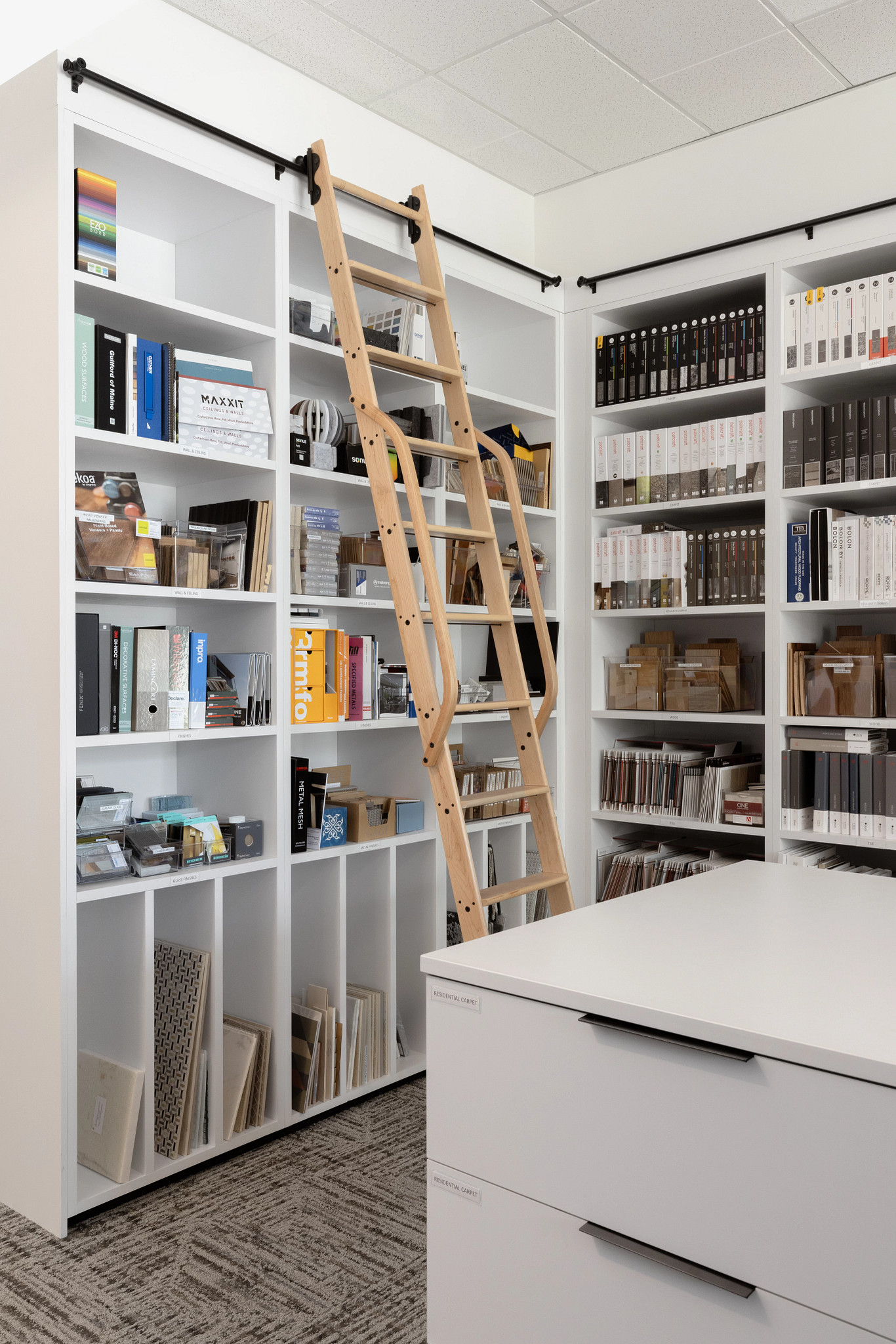 Workplace library with wooden ladder and shelves filled with flooring samples, featuring 18x36 inch commercial carpet tile