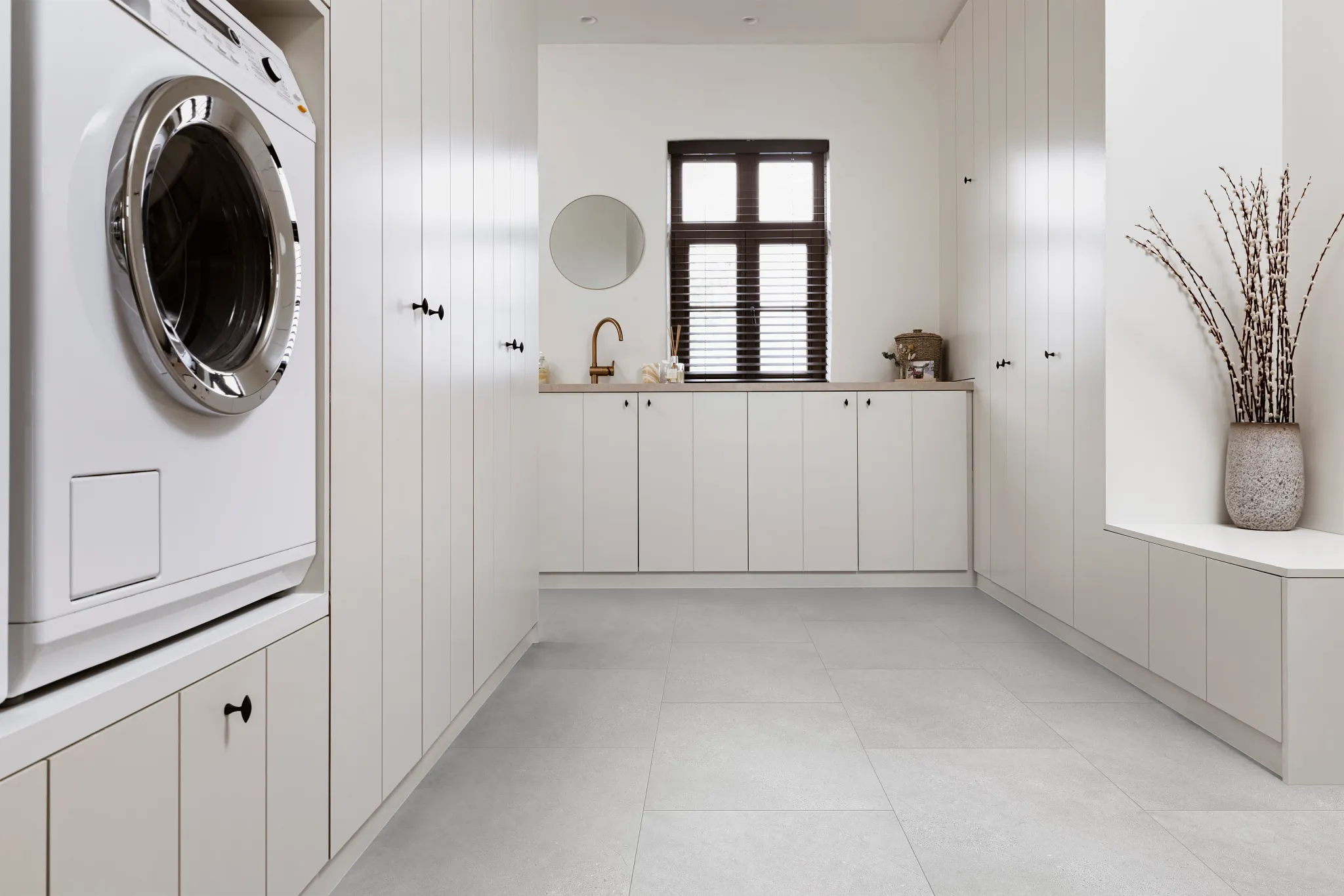 Modern laundry room with light gray luxury vinyl tile flooring, white cabinetry, and a washing machine