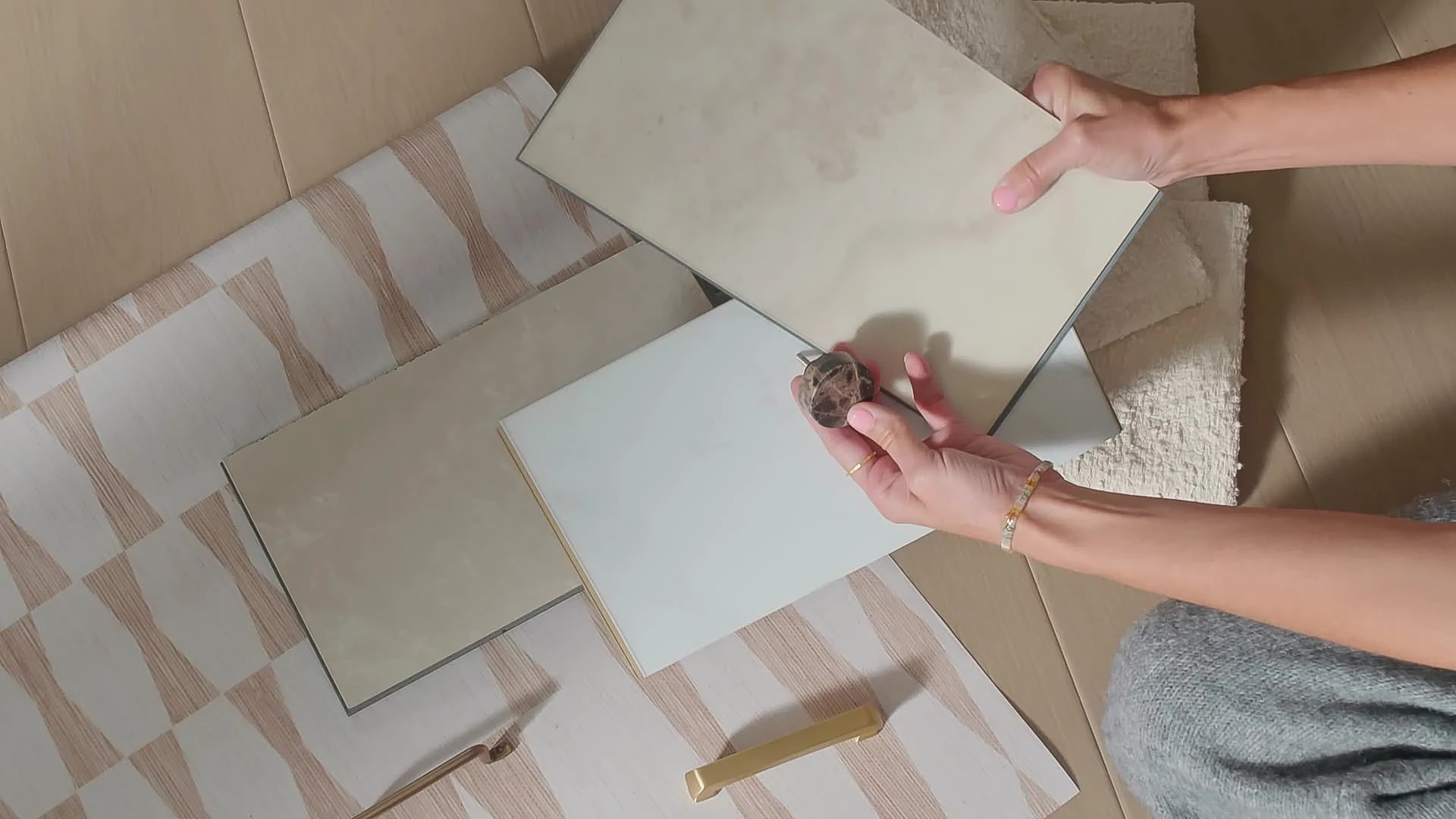 Person holding beige and cream vinyl tile samples on a patterned rug