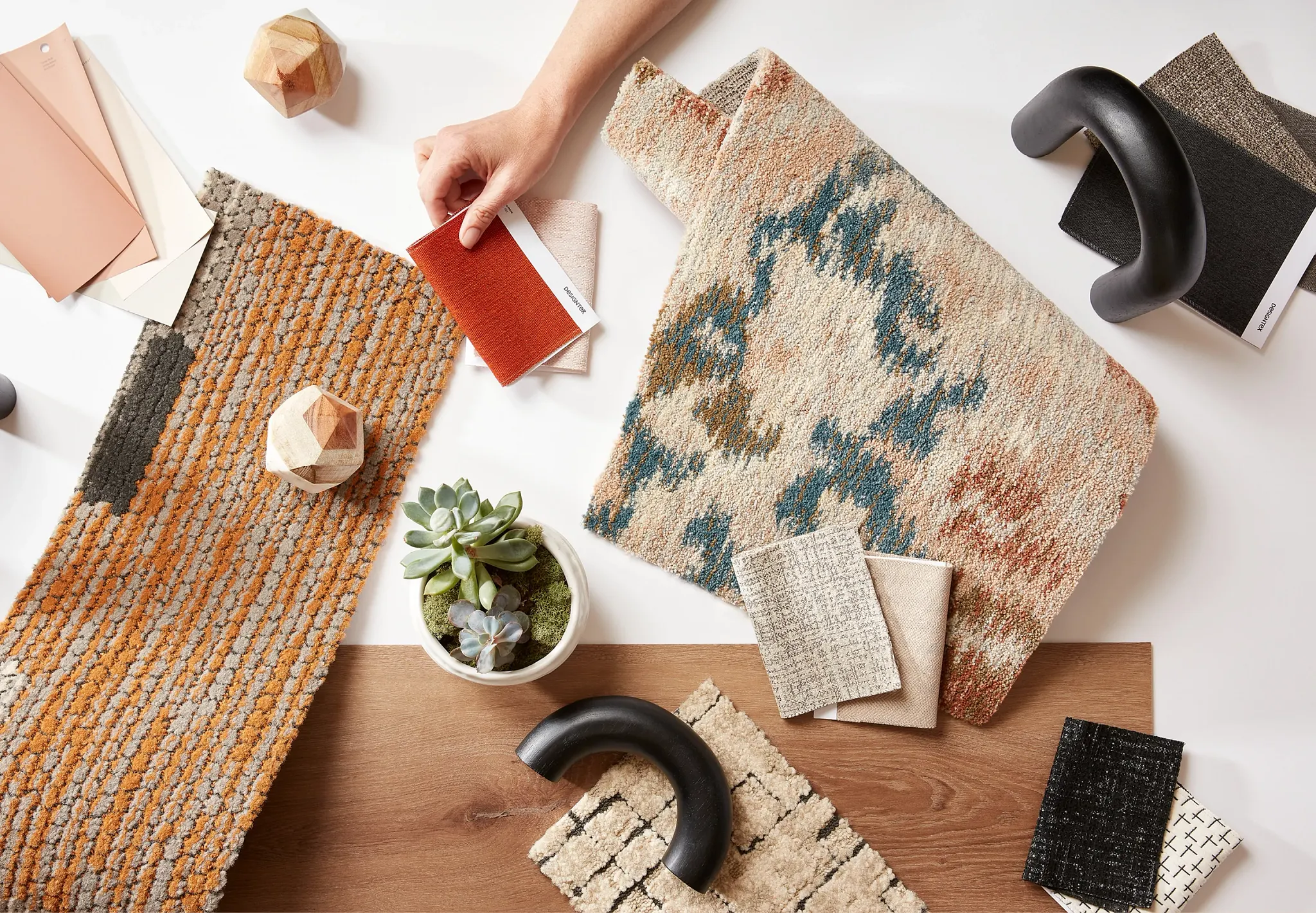 Assorted carpet swatches in orange, beige, and blue tones with a hand selecting a red fabric sample, surrounded by design elements and a small plant