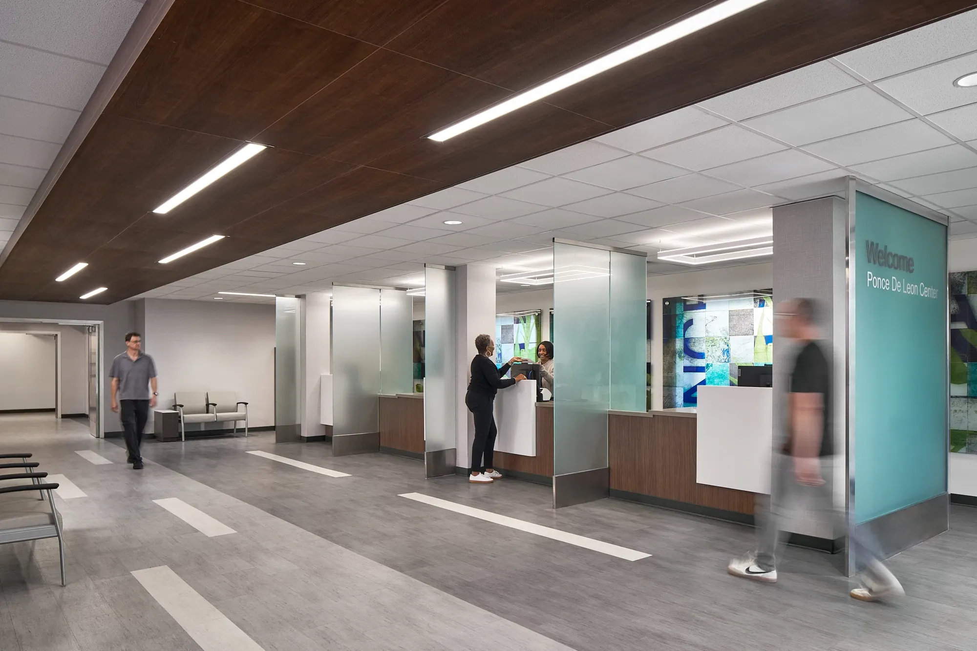 Modern healthcare facility lobby with commercial LVT flooring in gray tones, featuring a reception area and people interacting