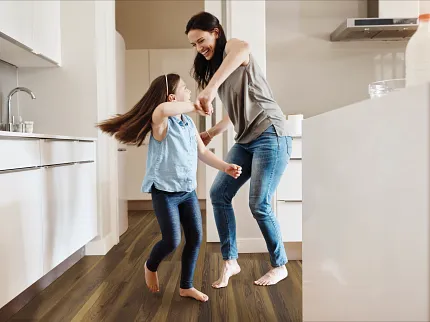 Coretec Residential WPC Luxury Vinyl Plank Flooring in Modern Kitchen - 48.03x7.05 inch kitchen with luxury vinyl plank floor in a wood look with a young woman and child dancing dimensions 4803x705 inch