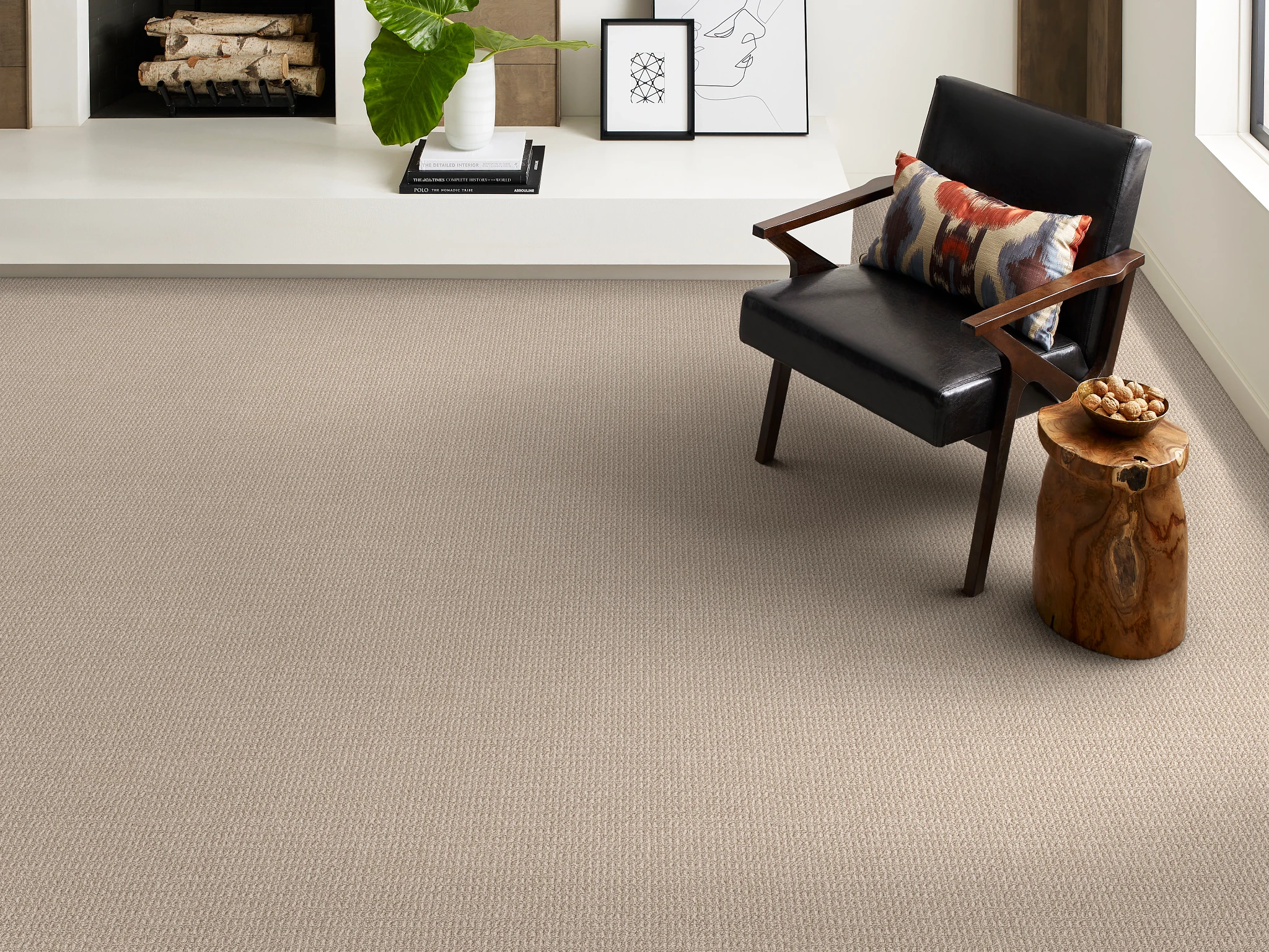 Modern living room with beige carpet flooring, featuring a black leather chair with a colorful pillow and a wooden side table