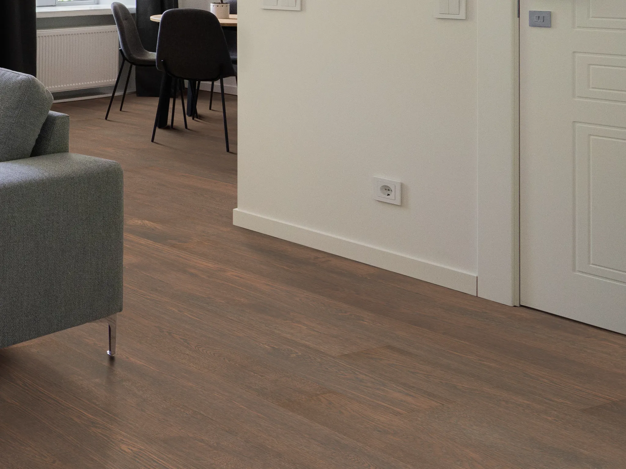 Cozy living room with dark wood-look laminate flooring, featuring a modern gray sofa and dining area