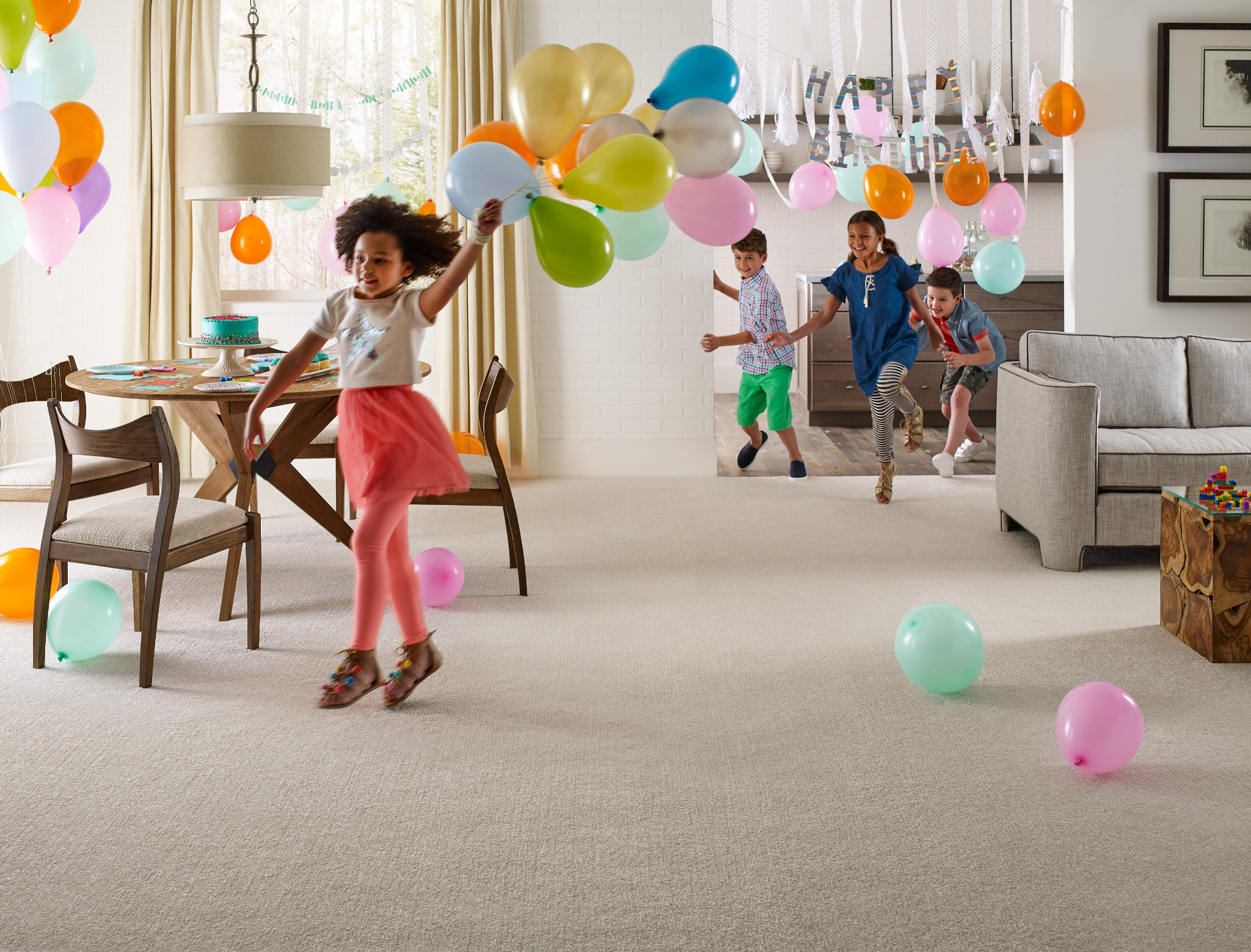 young girl running with balloons through a living room with Shaw carpet being chased by other laughing children at a birthday party 