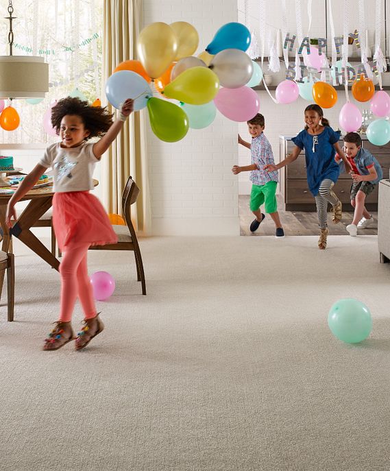 young girl running with balloons through a living room with Shaw carpet being chased by other laughing children at a birthday party 