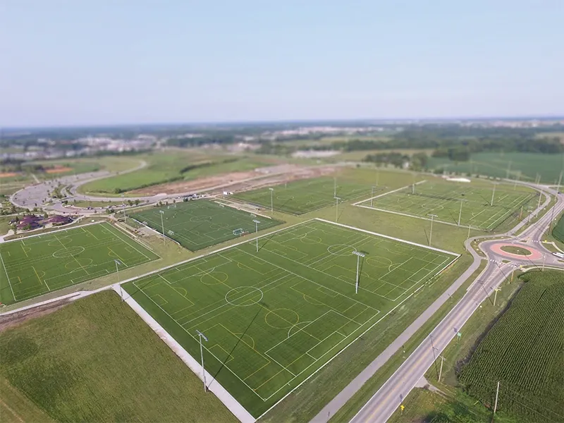 Aerial view of multiple sports fields with artificial turf surrounded by roads and greenery