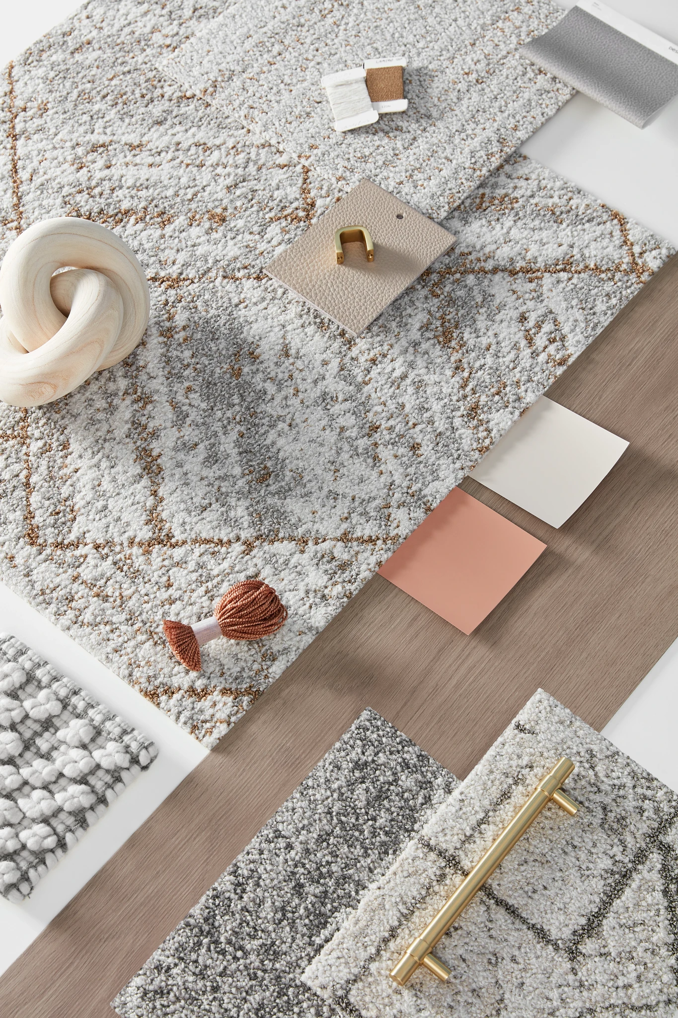 Swatch of commercial carpet tiles in shades of gray, white, and beige with textured patterns, accompanied by design elements like a brass handle and c