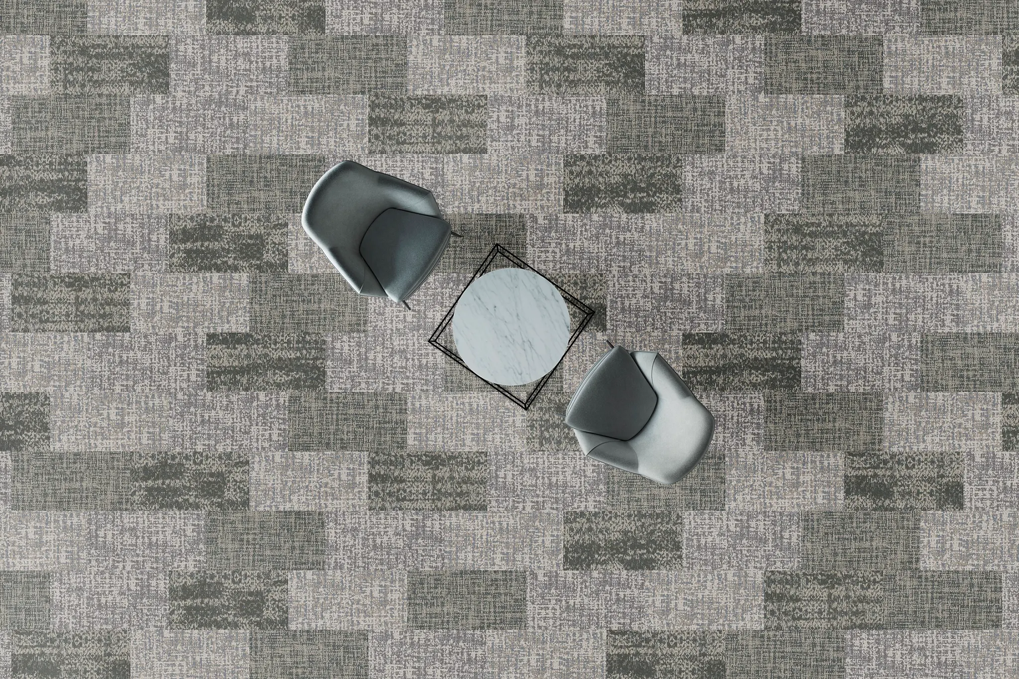 Overhead view of a modern office space with two gray chairs and a small marble-top table on a patterned gray and green commercial carpet tile floor