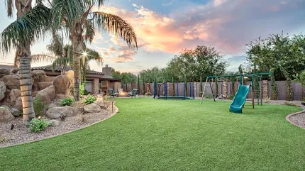 Beautiful outdoor space with synthetic turf and play area Backyard with artificial grass and playground at sunset