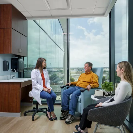 Healthcare Facility Room with Light Wood Flooring and Consultation Setting Healthcare facility room with light wood flooring, featuring a healthcare professional and two individuals seated in a consultation setting