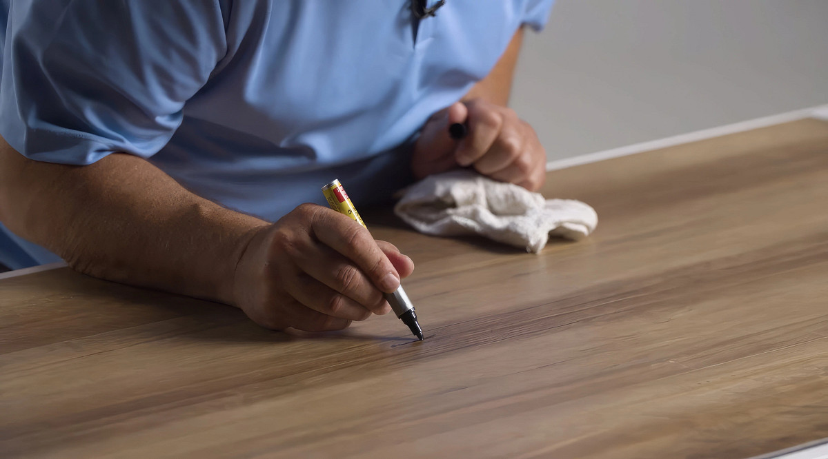 man fixing a scratch in flooring with a paint pen