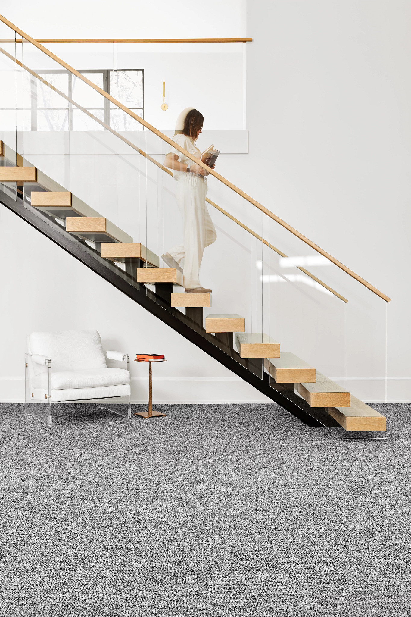 Modern staircase with glass railing and wooden steps in a contemporary interior featuring gray commercial carpet flooring