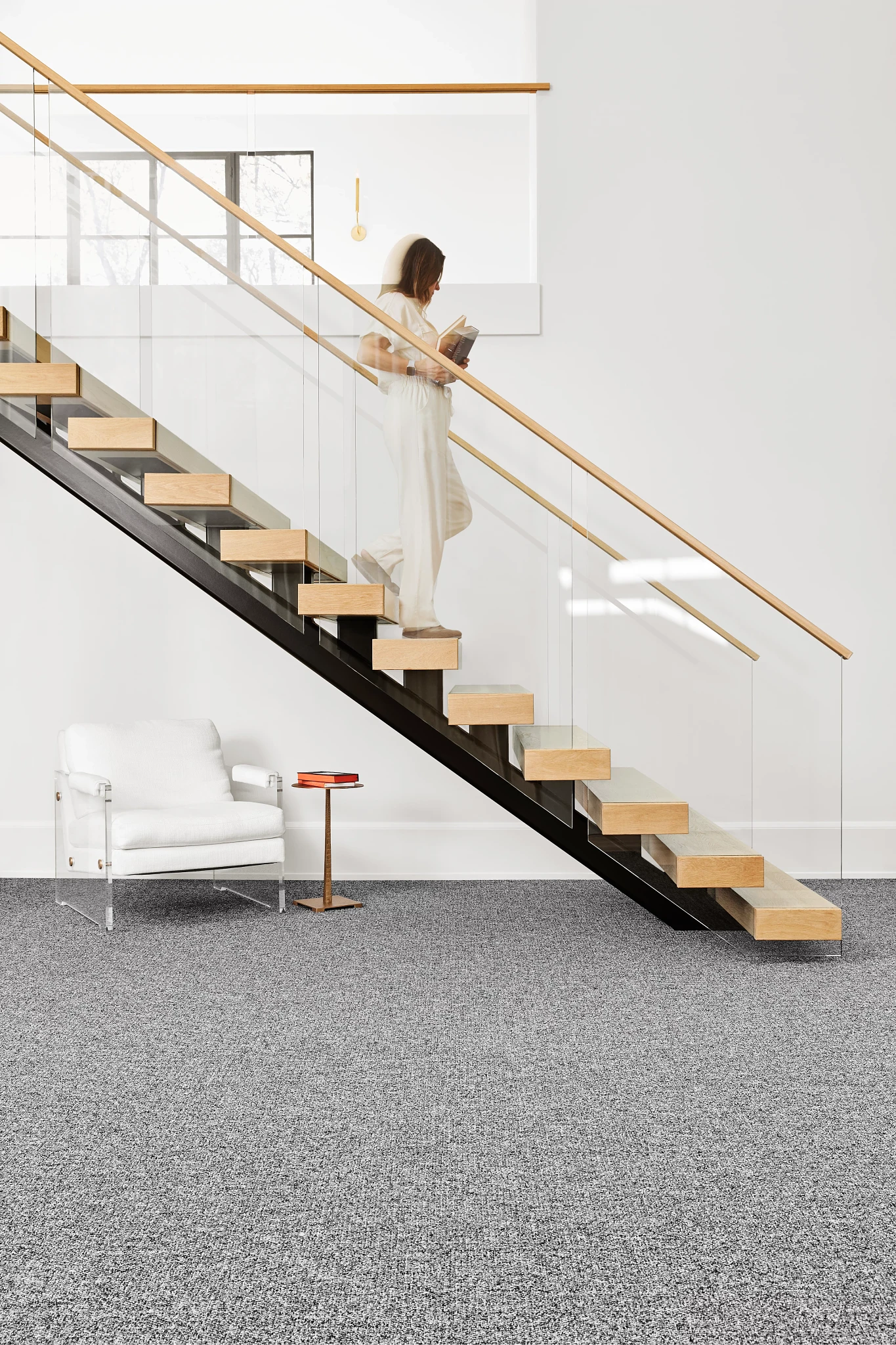 Modern staircase with glass railing and wooden steps in a contemporary interior featuring gray commercial carpet flooring