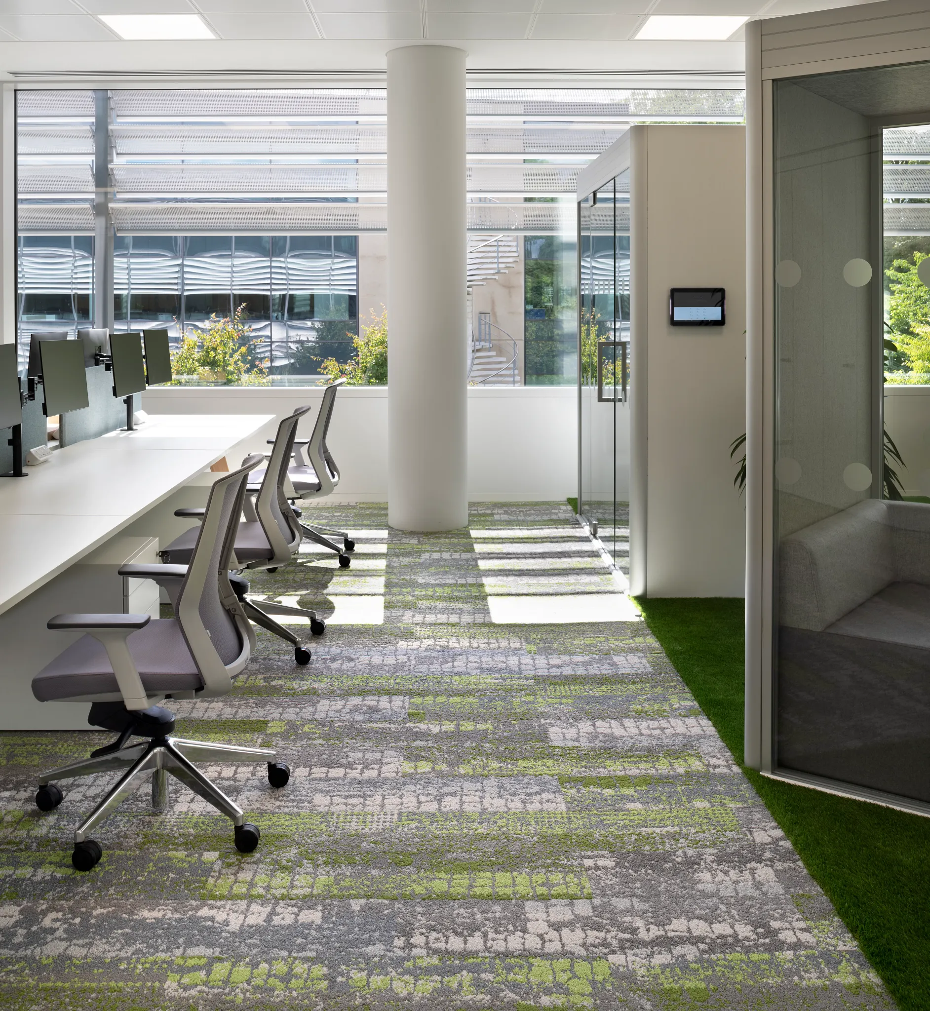 Modern office space with large windows and ergonomic chairs on a patterned commercial carpet tile in shades of gray and green