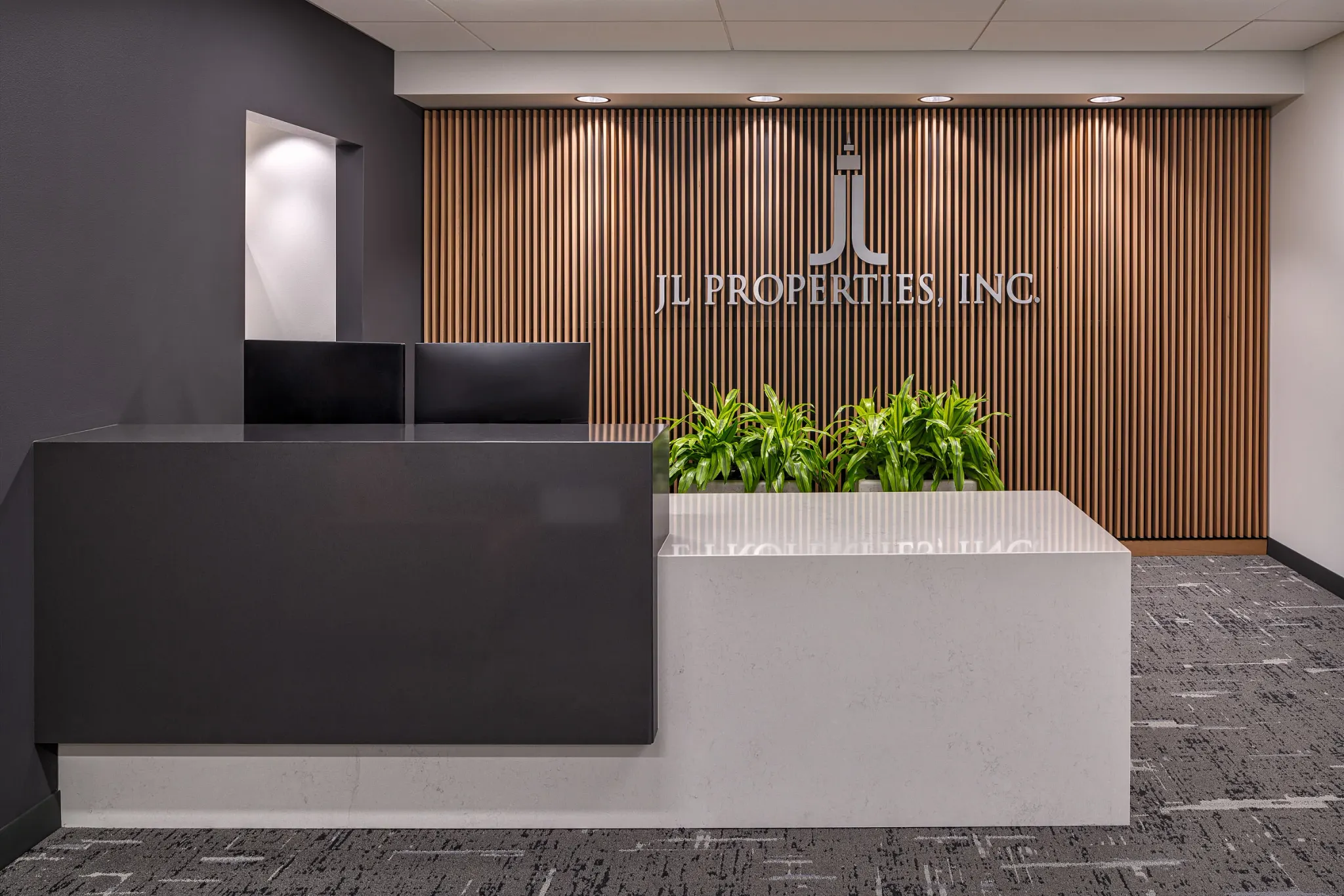 Modern office reception area with sleek black and white desk, wooden slat wall, and commercial carpet tile flooring