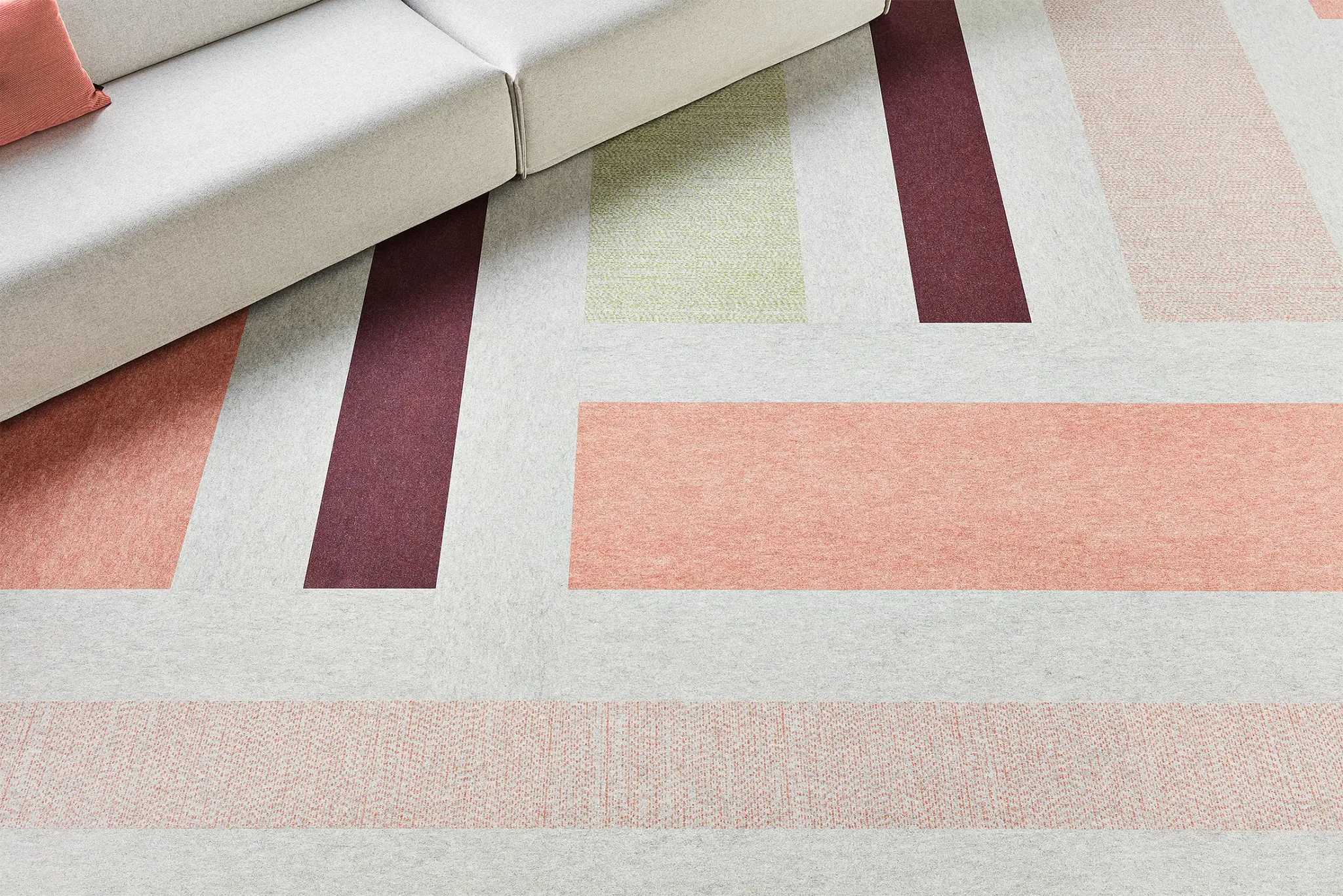 Modern living room with geometric pattern carpet in shades of grey, peach, burgundy, and green, featuring a light grey sofa with a coral cushion