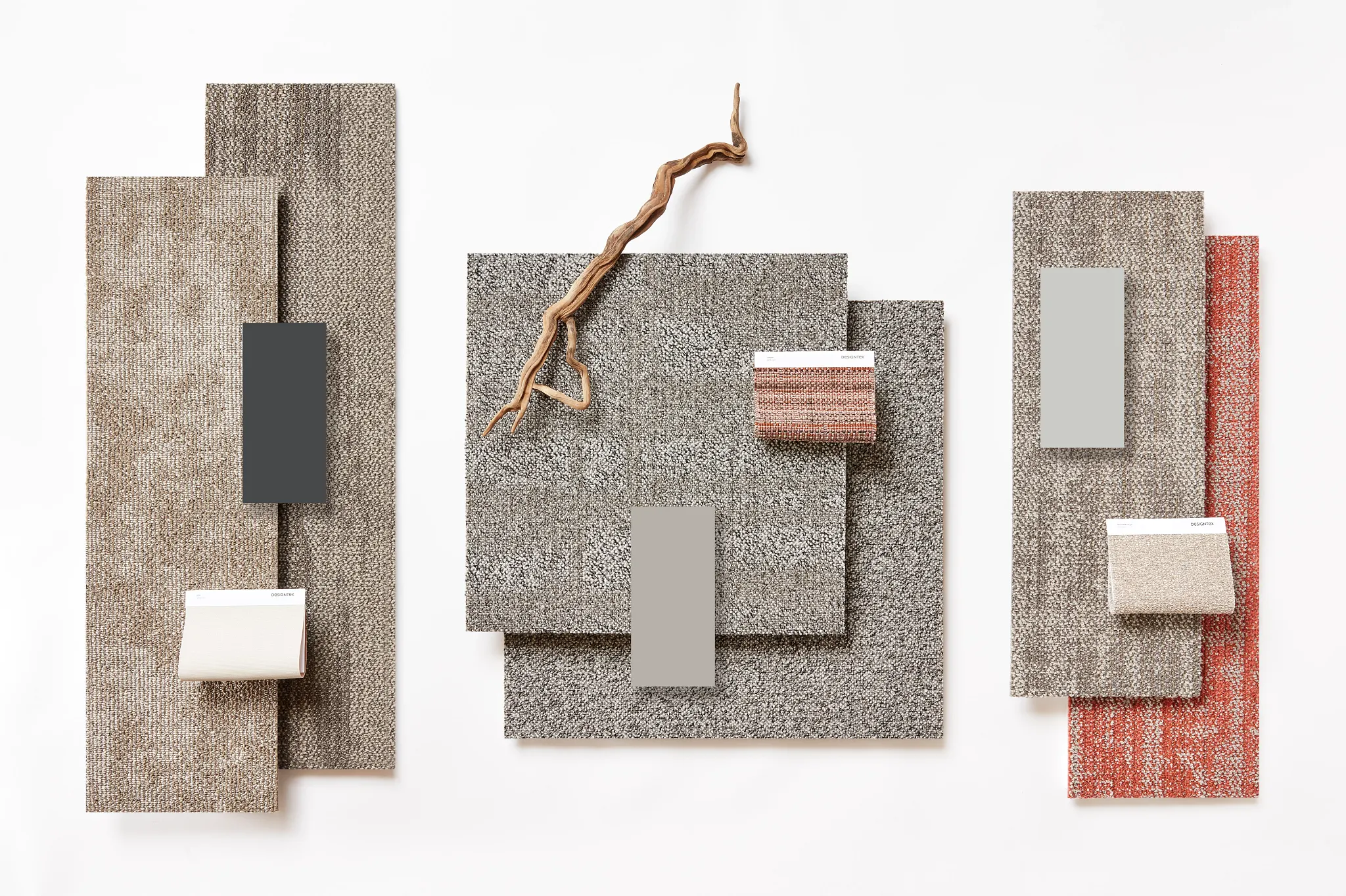 Swatch of commercial carpet tiles in shades of beige, gray, and red with a decorative twig