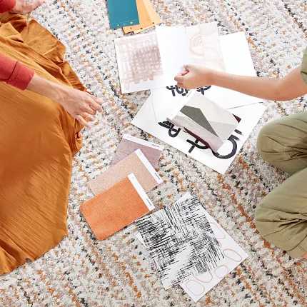Interior design planning with fabric and color swatches on textured carpet Two women sitting on a textured carpet with various fabric and color swatches