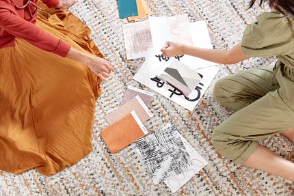 Interior design planning with fabric and color swatches on textured carpet Two women sitting on a textured carpet with various fabric and color swatches